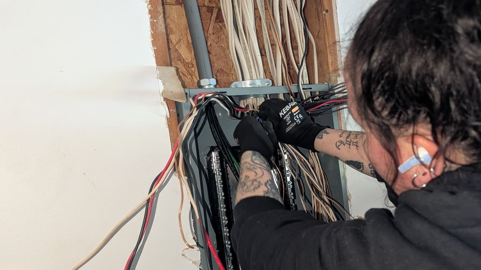Electrician working on wiring inside an open electrical panel in a wall