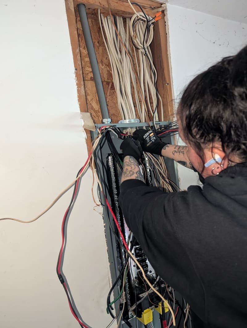 Electrician working inside an open electrical panel wall