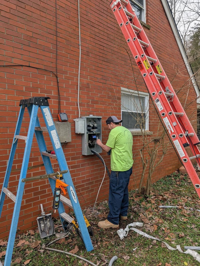 Electrician working on exterior meter panel beside ladders